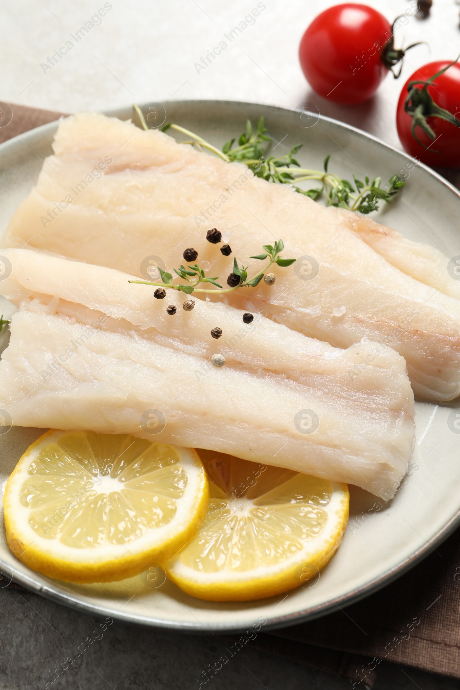 Photo of Plate with raw cod fish, spices, microgreens and lemon on grey table, closeup