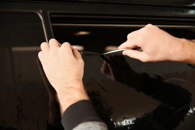 Photo of Worker tinting car window in shop, closeup