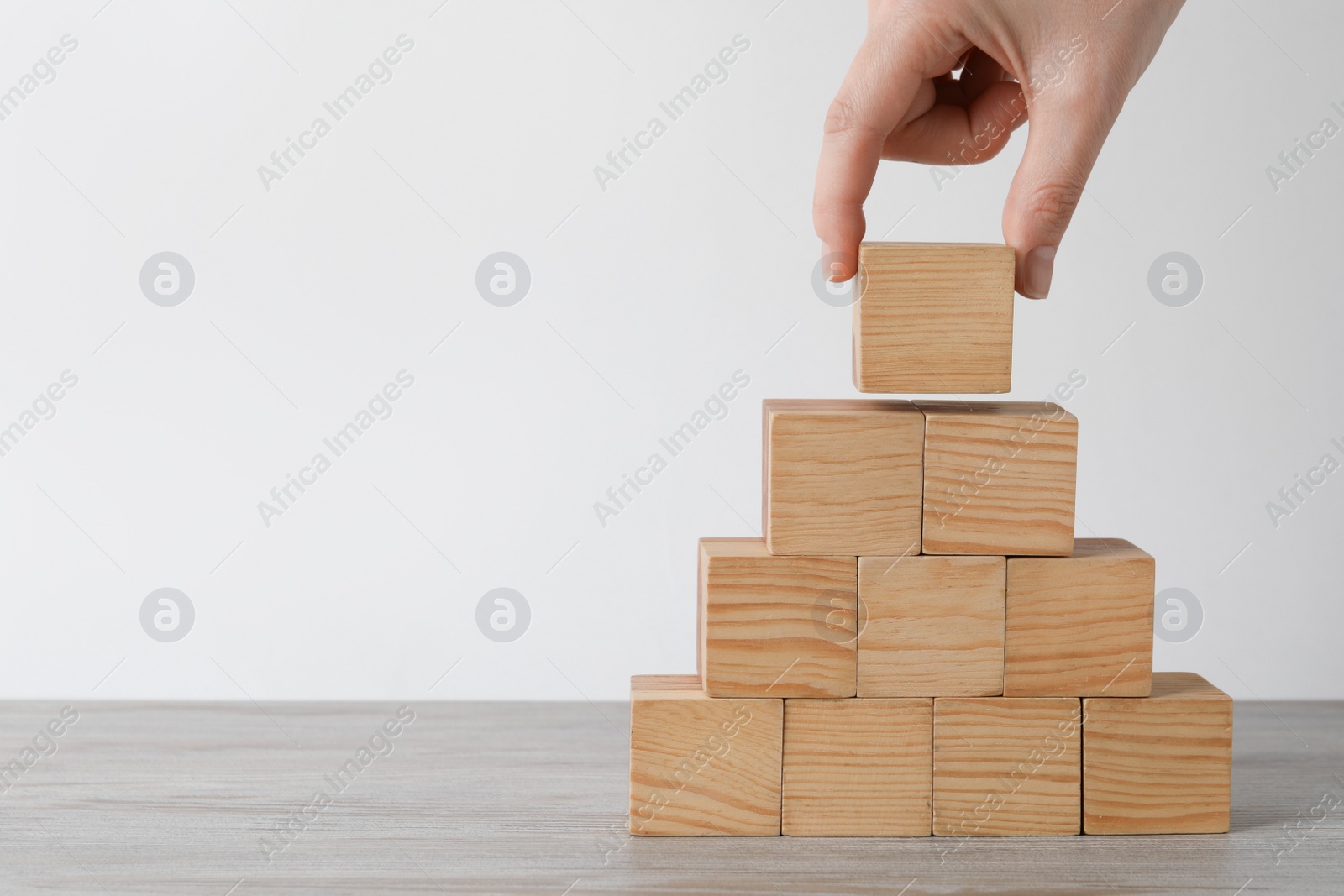 Photo of Woman building pyramid with wooden cubes at table, closeup and space for text. Management concept