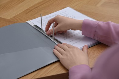 Photo of Woman fixing folder with punched pockets at wooden table, closeup