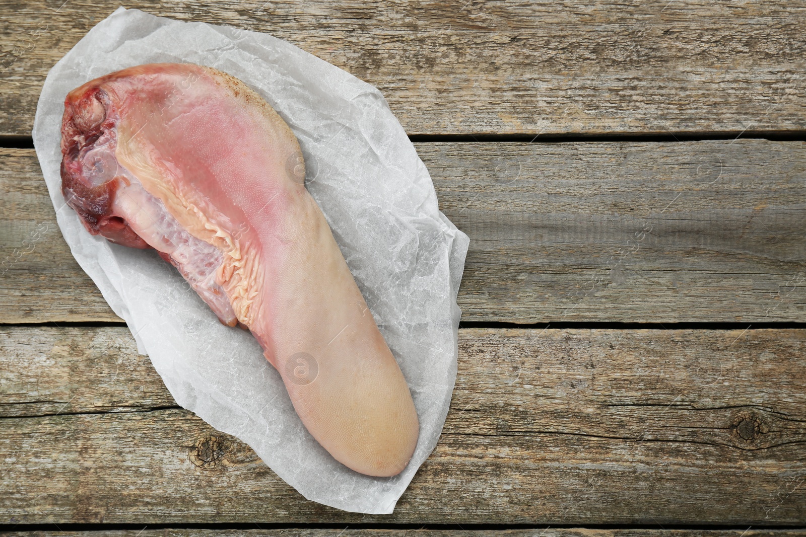 Photo of Parchment with raw beef tongue on wooden table, top view. Space for text