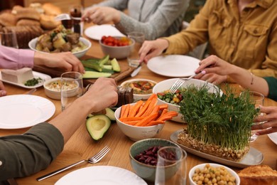 Friends eating vegetarian food at wooden table indoors, closeup