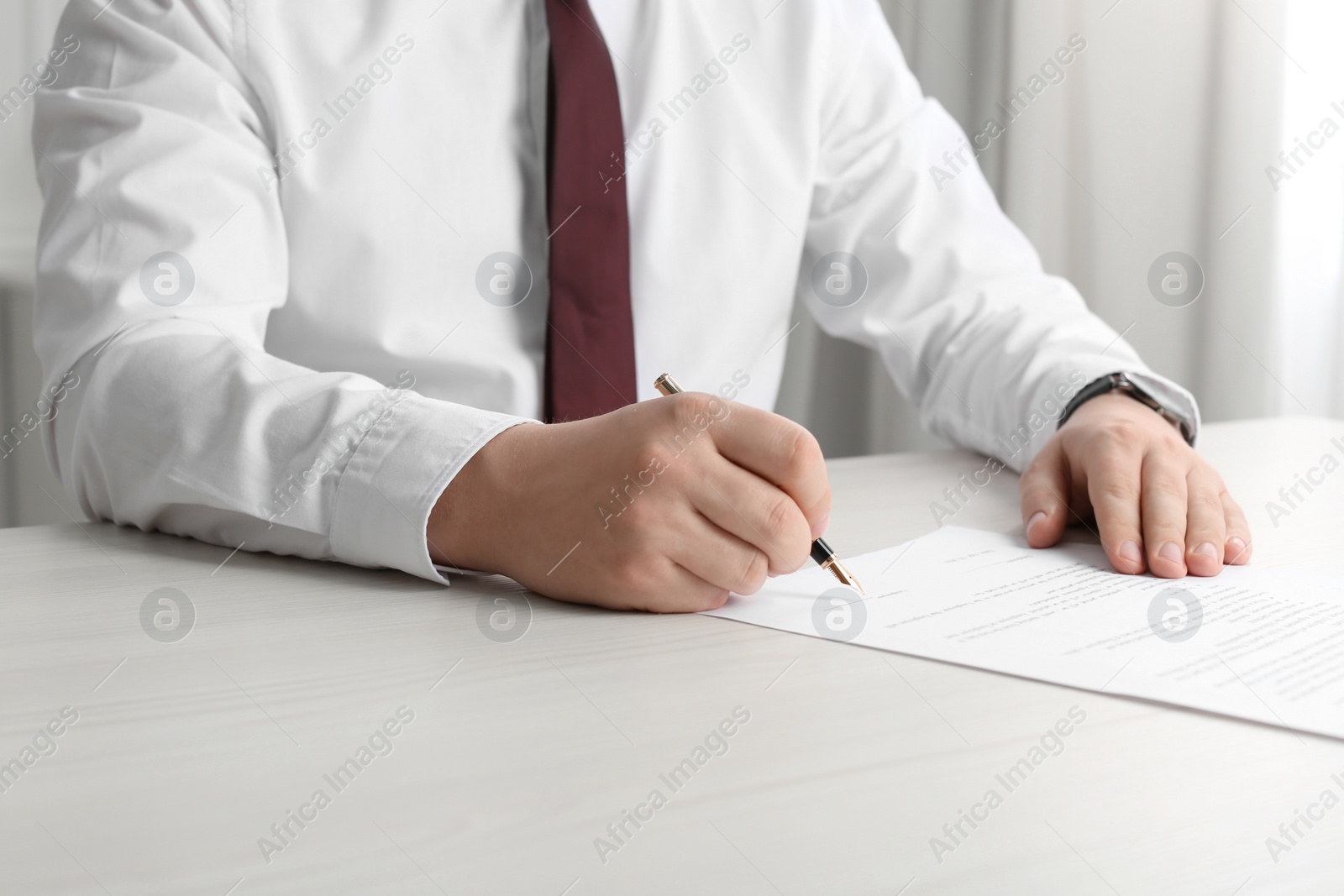 Photo of Notary signing document at wooden table indoors, closeup