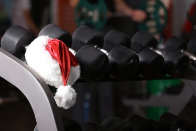 Photo of Santa Claus hat on stand with dumbbells in gym