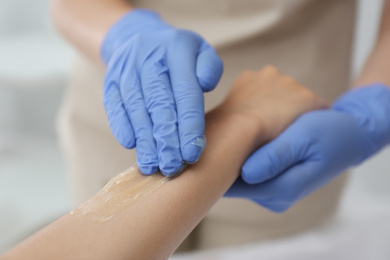 Photo of Woman getting wax epilation of arm in salon, closeup