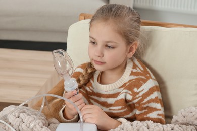 Photo of Little girl holding nebulizer for inhalation in armchair at home