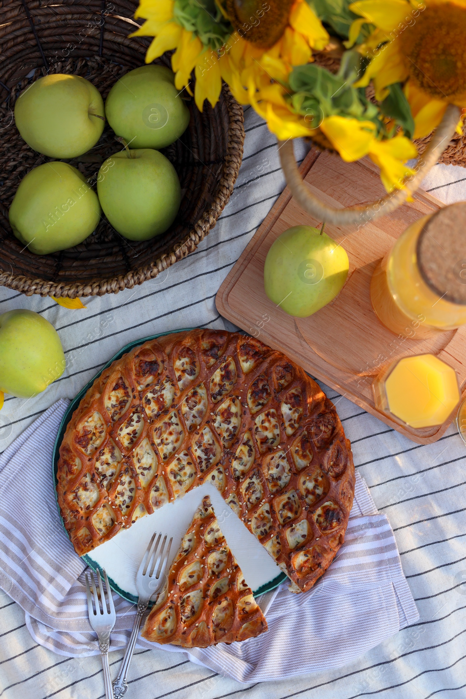 Photo of Delicious pie, apples and juice on striped blanket outdoors, flat lay. Picnic season