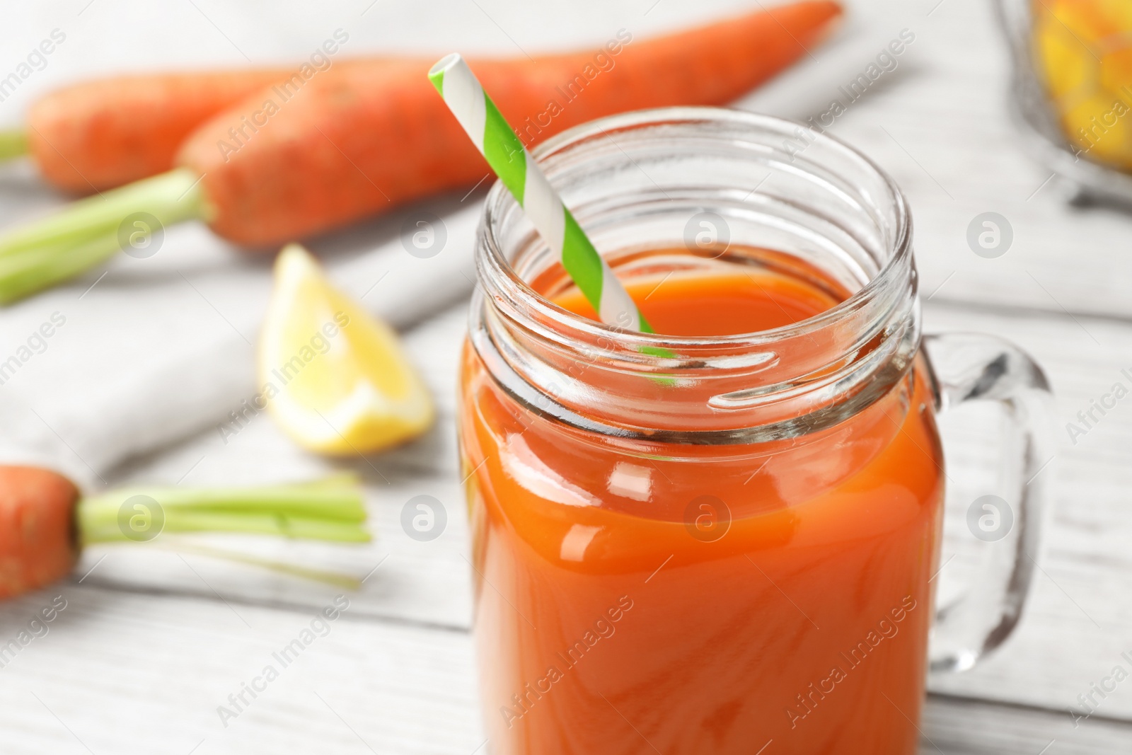 Photo of Mason jar with fresh carrot juice on white wooden table, space for text