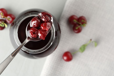 Spoon of pickled cherries above table, top view