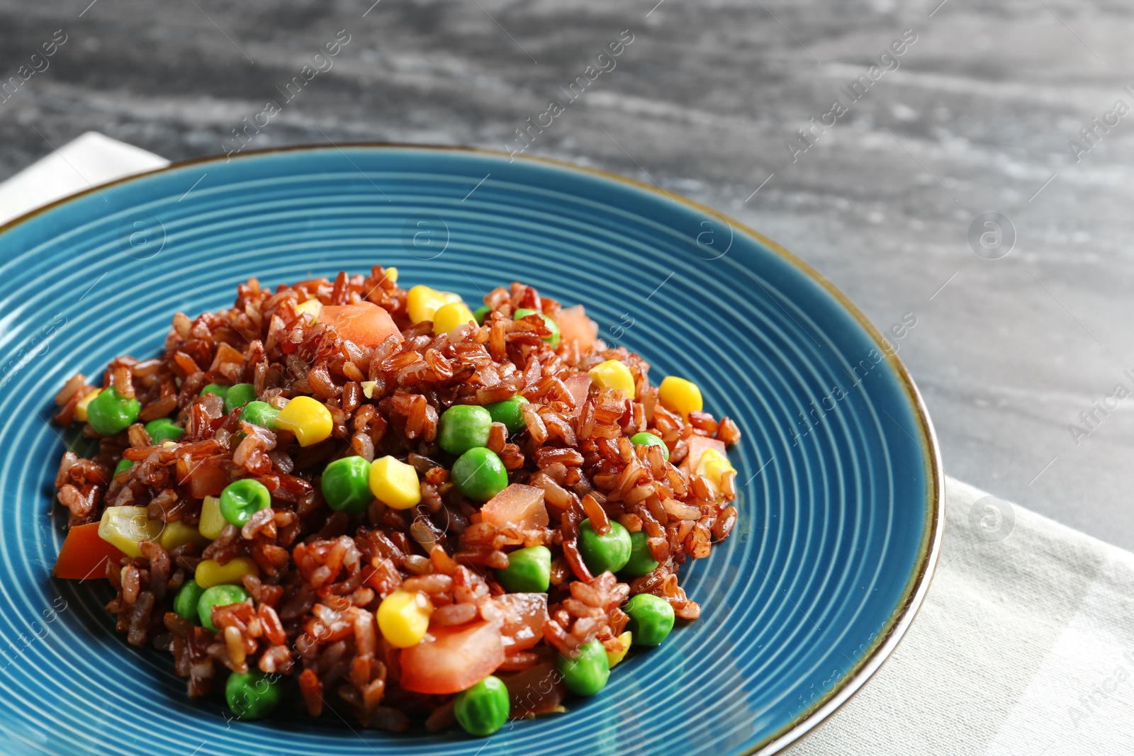 Photo of Plate of boiled brown rice with vegetables on table, closeup. Space for text