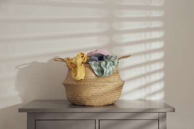 Wicker laundry basket with different clothes on chest of drawers indoors