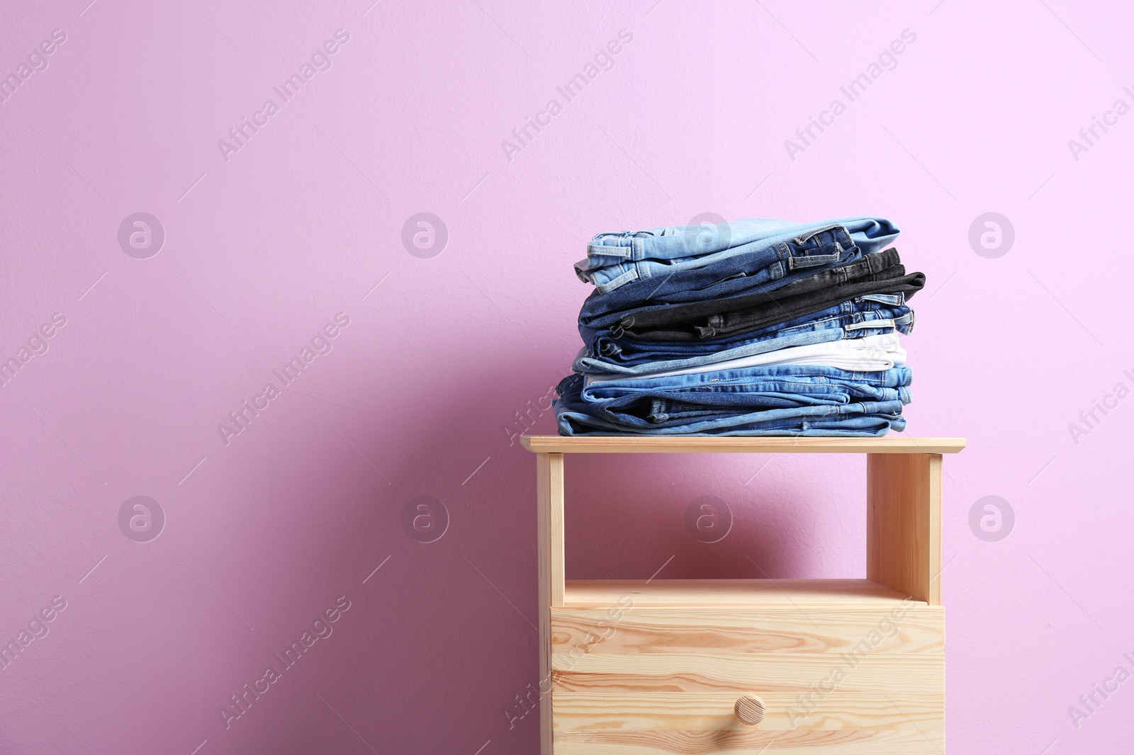 Photo of Stack of different jeans on table against color background