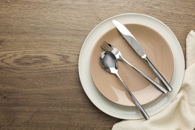 Photo of Clean plates and cutlery on wooden table, top view. Space for text