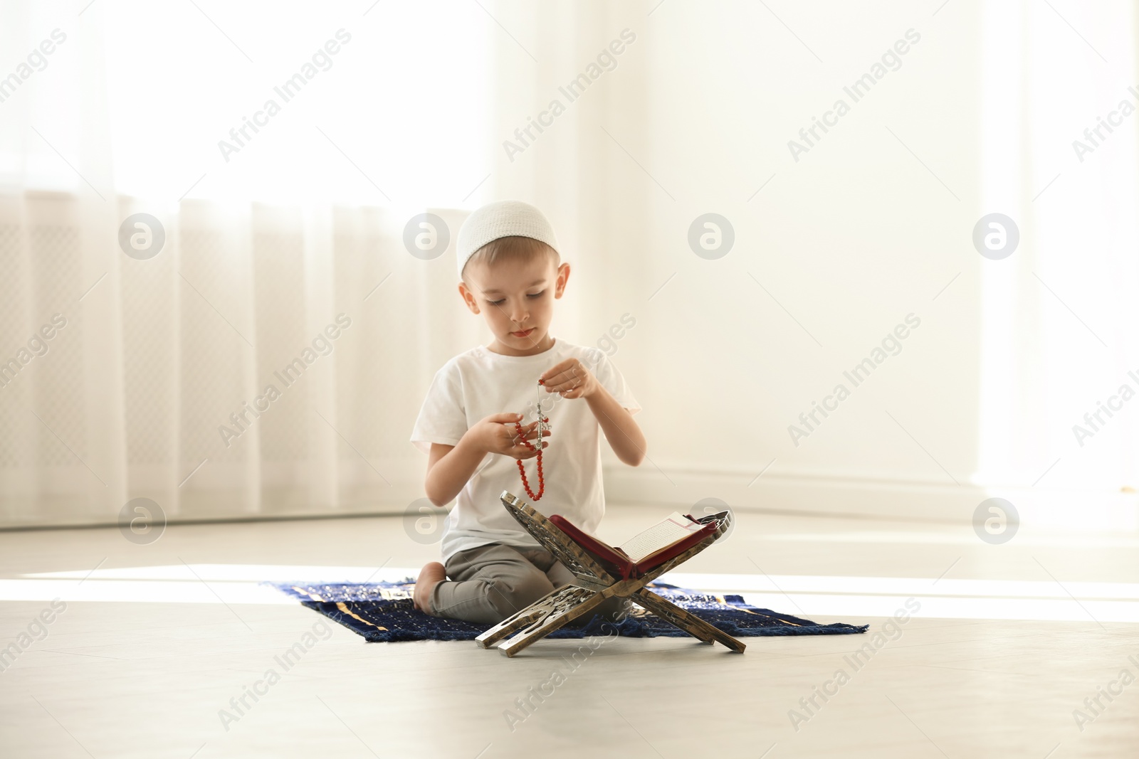 Photo of Little Muslim boy with misbaha and Koran praying on rug indoors