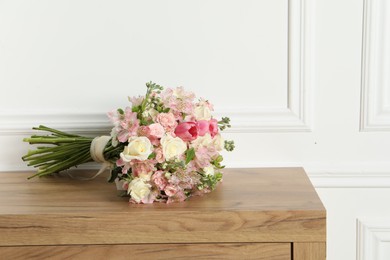 Beautiful bouquet of fresh flowers on wooden table near white wall, space for text