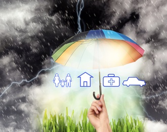 Image of Insurance concept. Woman protecting illustrations with rainbow umbrella from storm, closeup