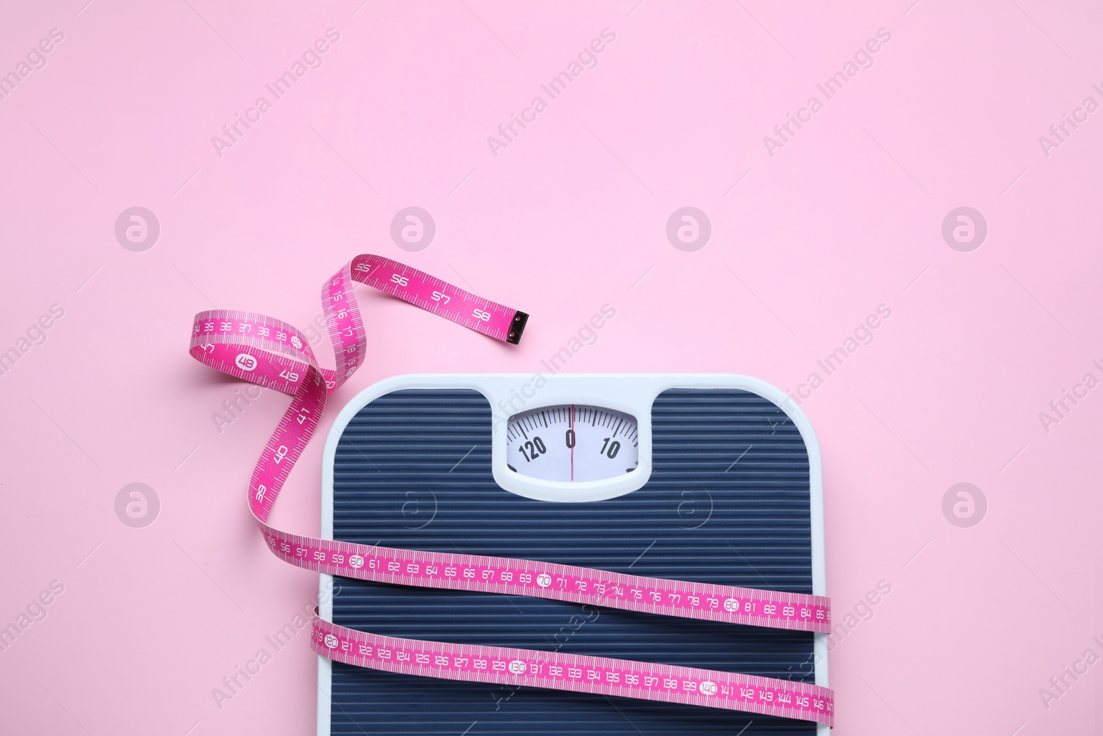 Photo of Scales and measuring tape on pink background, top view. Space for text