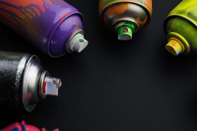 Photo of Used cans of spray paints on black background, closeup with space for text. Graffiti supplies