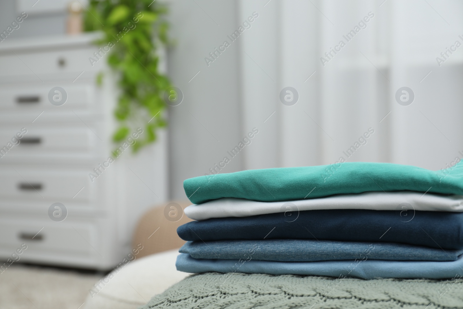 Photo of Sorting and organizing. Stack of different folded clothes on bed indoors, space for text