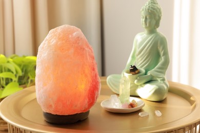 Photo of Himalayan salt lamp, buddha figure and crystals on golden table indoors