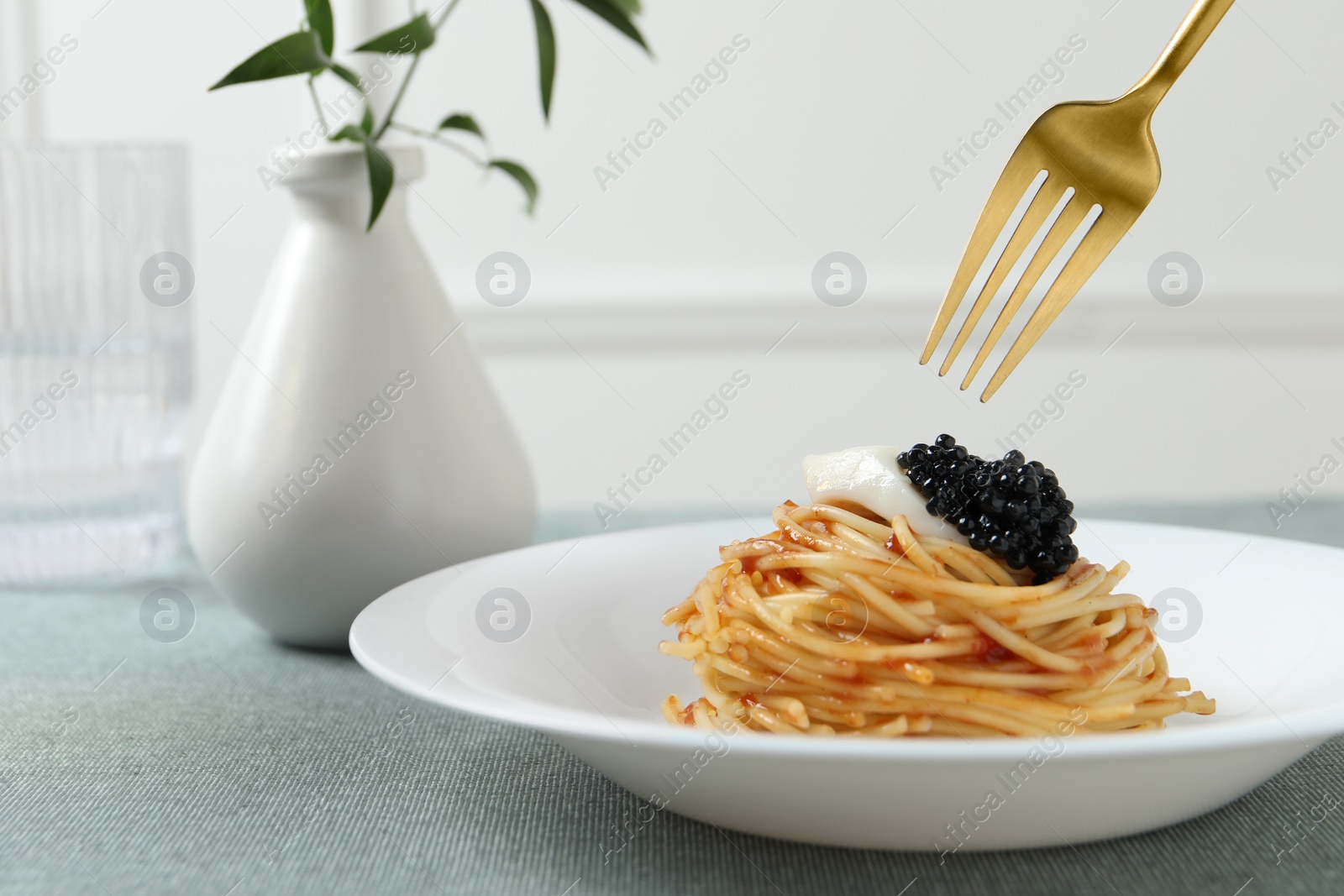 Photo of Eating tasty spaghetti with tomato sauce and black caviar at table, closeup. Exquisite presentation of pasta dish