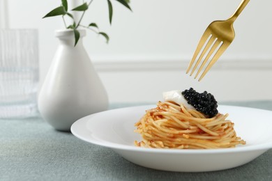 Eating tasty spaghetti with tomato sauce and black caviar at table, closeup. Exquisite presentation of pasta dish