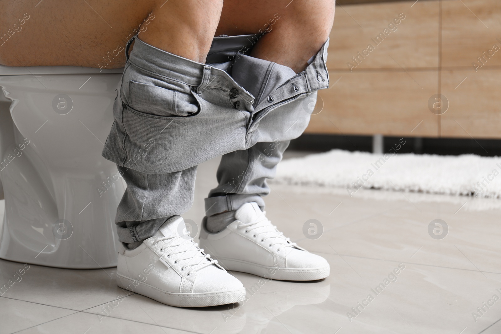 Photo of Man sitting on toilet bowl in bathroom, closeup