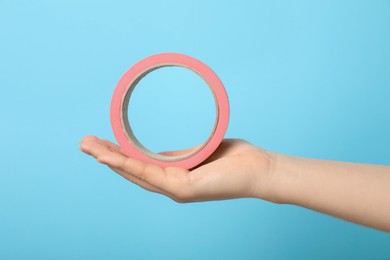 Photo of Woman holding pink adhesive tape on light blue background, closeup