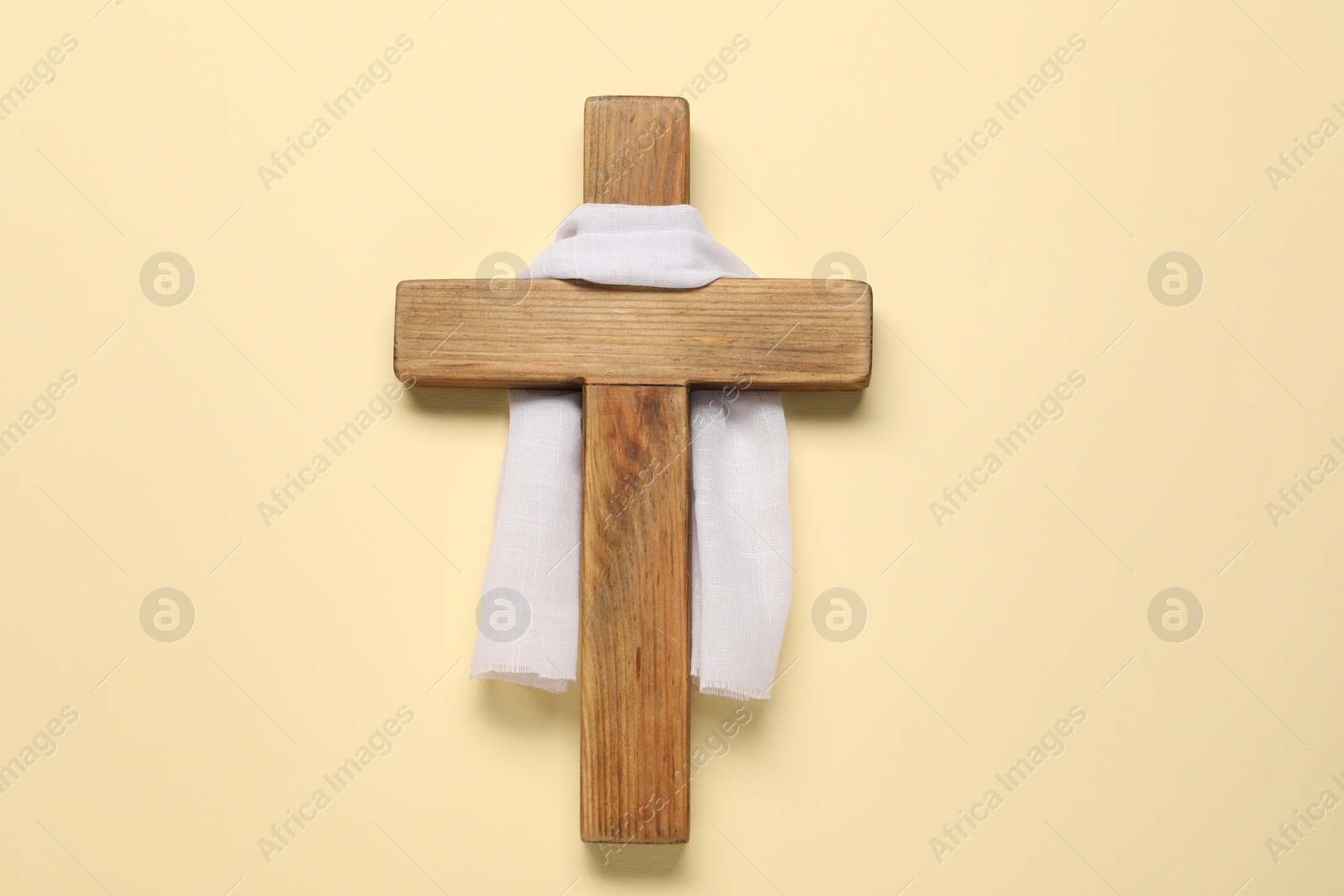 Photo of Wooden cross and white cloth on beige background, top view. Easter attributes