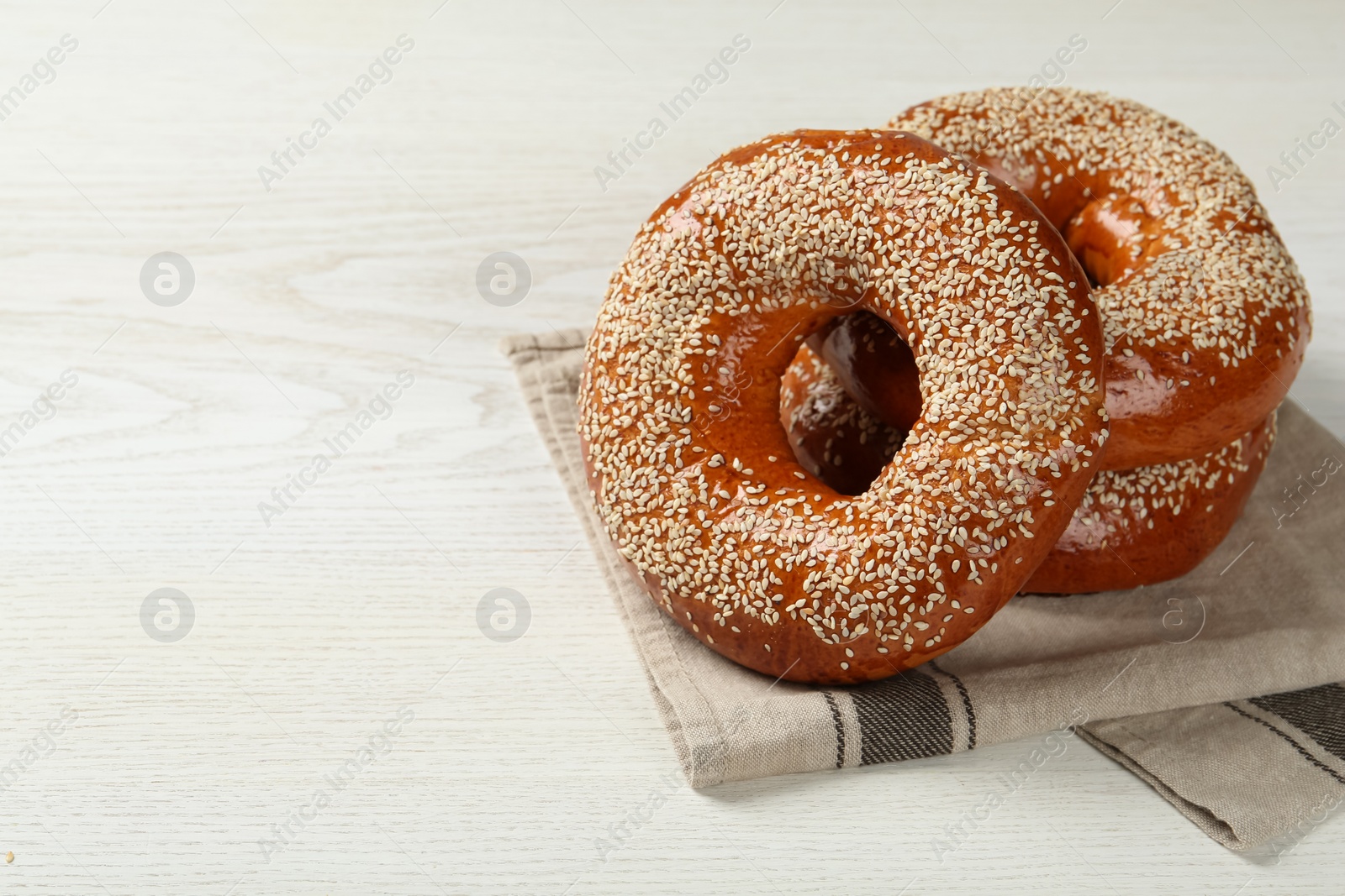 Photo of Delicious fresh bagels with sesame seeds on white wooden table, space for text
