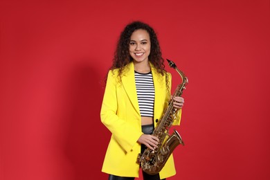 Beautiful African American woman with saxophone on red background