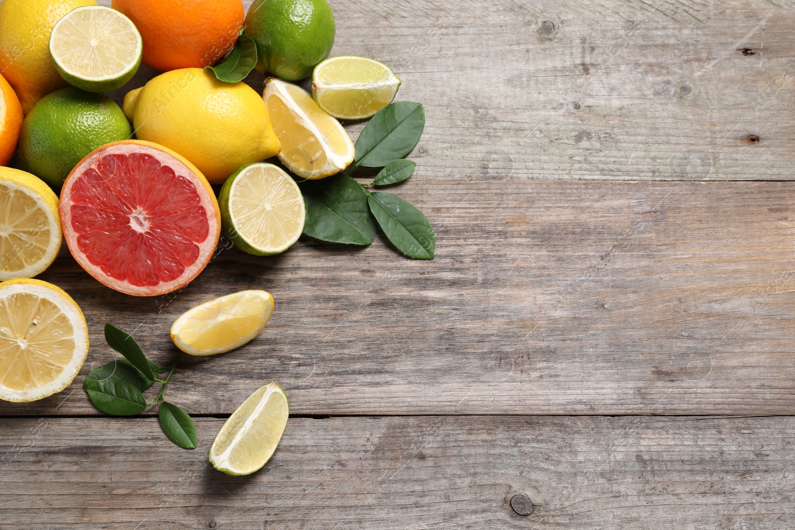 Photo of Different fresh citrus fruits and leaves on wooden table, flat lay. Space for text