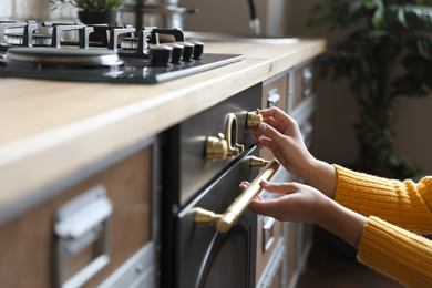 Photo of Woman using modern oven in kitchen, closeup