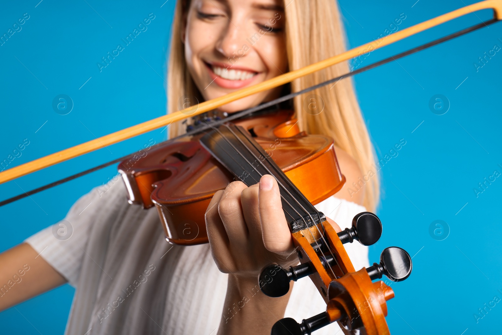 Photo of Beautiful woman playing violin on light blue background, closeup