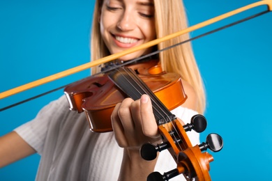 Beautiful woman playing violin on light blue background, closeup