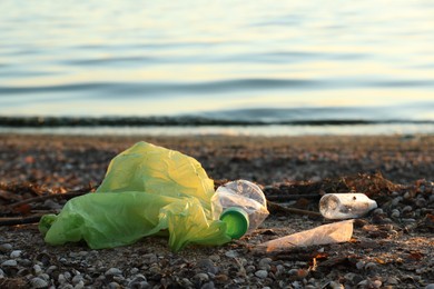 Photo of Plastic bag and bottles on sand near water. Environment pollution