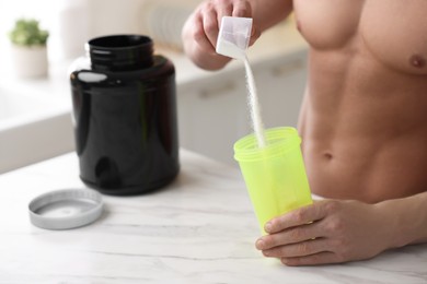 Young muscular man making protein shake at white marble table in kitchen, closeup