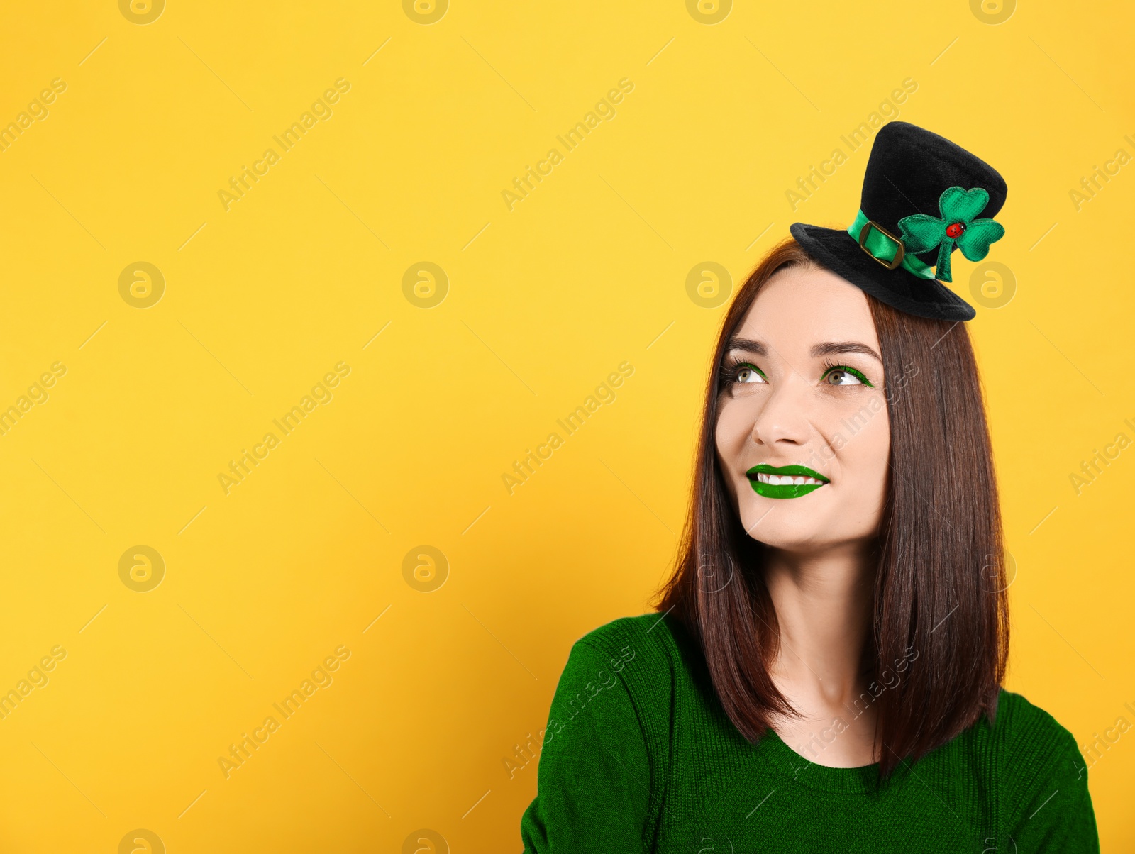 Image of St. Patrick's day party. Pretty woman with green lips in leprechaun hat on golden background. Space for text