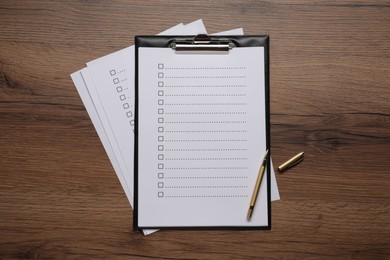 Photo of Clipboard with checkboxes and pen on wooden table, flat lay
