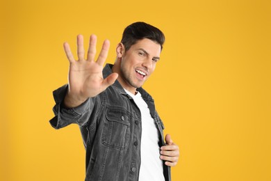 Man showing number five with his hand on yellow background