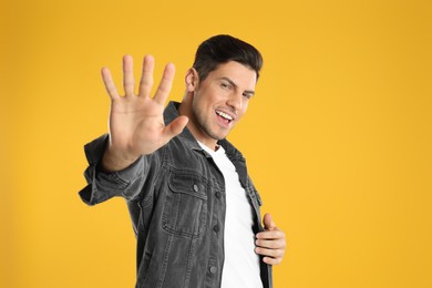 Photo of Man showing number five with his hand on yellow background