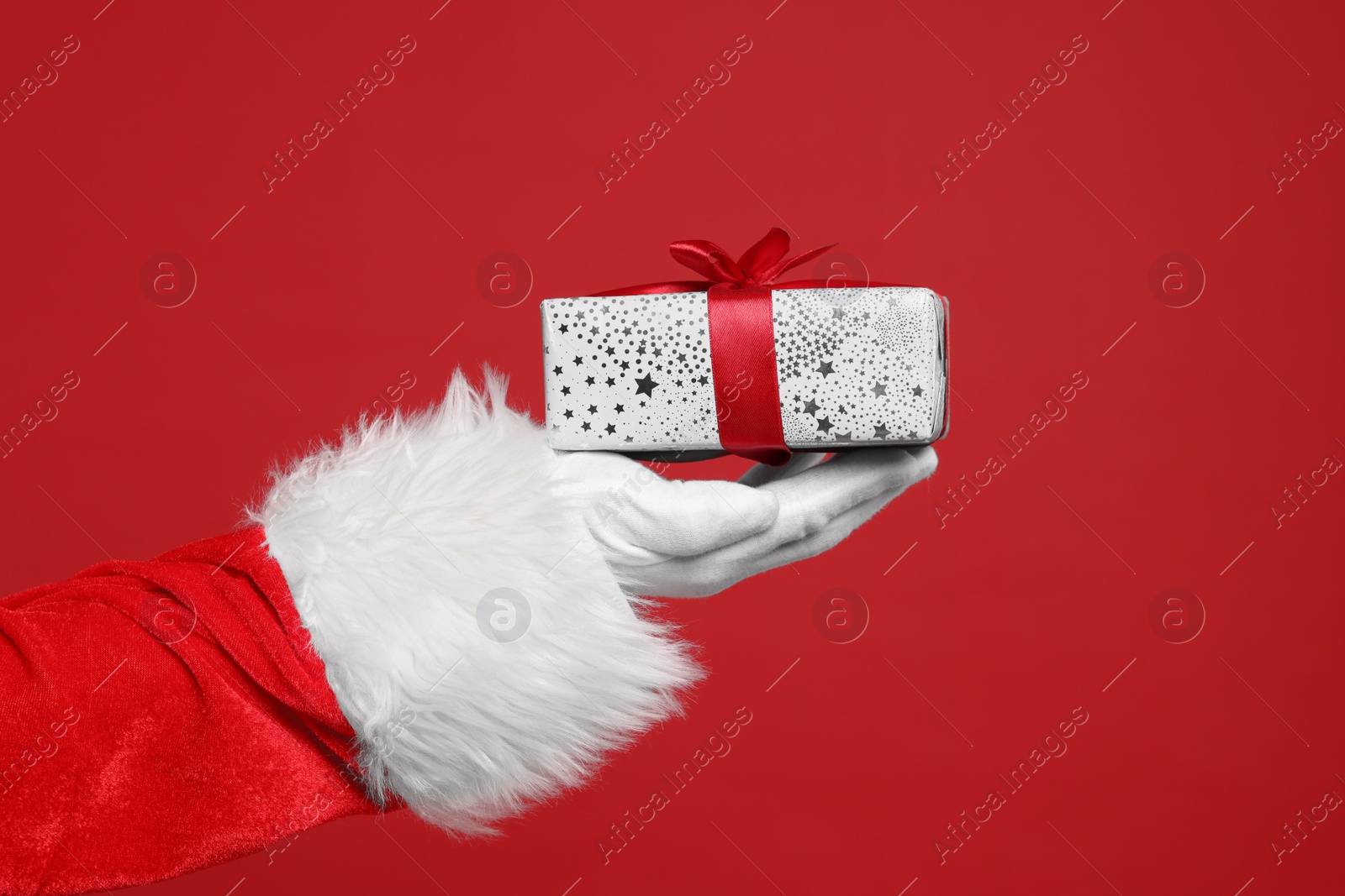 Photo of Santa Claus holding Christmas gift on red background, closeup