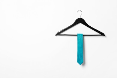 Photo of Hanger with light blue necktie on white wall. Space for text
