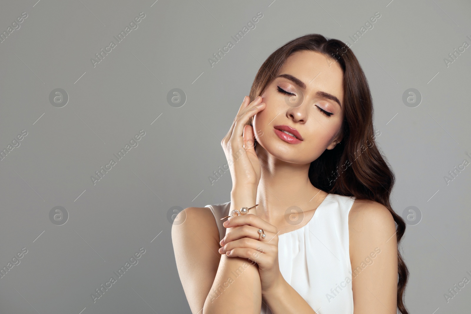 Photo of Young woman wearing elegant pearl jewelry on grey background, space for text