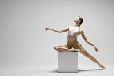Photo of Young ballerina practicing dance moves on cube against white background. Space for text