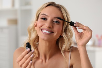 Photo of Beautiful makeup. Smiling woman applying mascara indoors