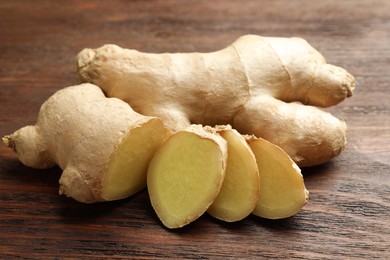 Photo of Cut and whole fresh ginger on wooden table, closeup