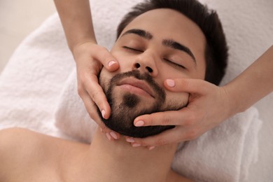 Photo of Young man receiving facial massage in beauty salon, above view