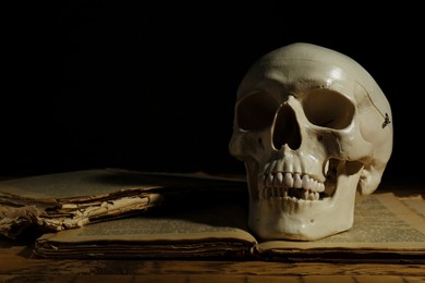 Human skull and old book on wooden table against black background. Space for text