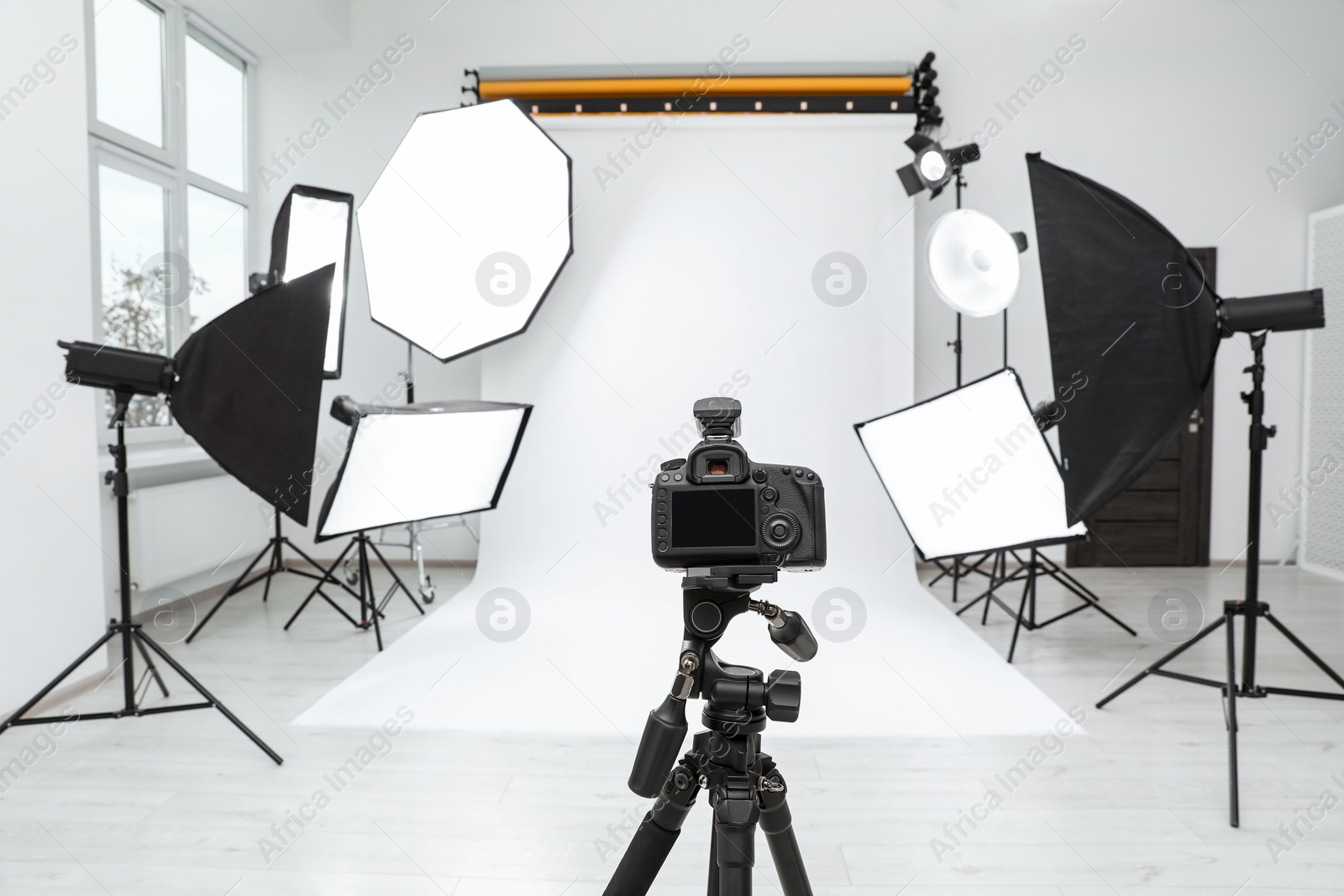 Photo of Tripod with camera and professional lighting equipment in modern photo studio